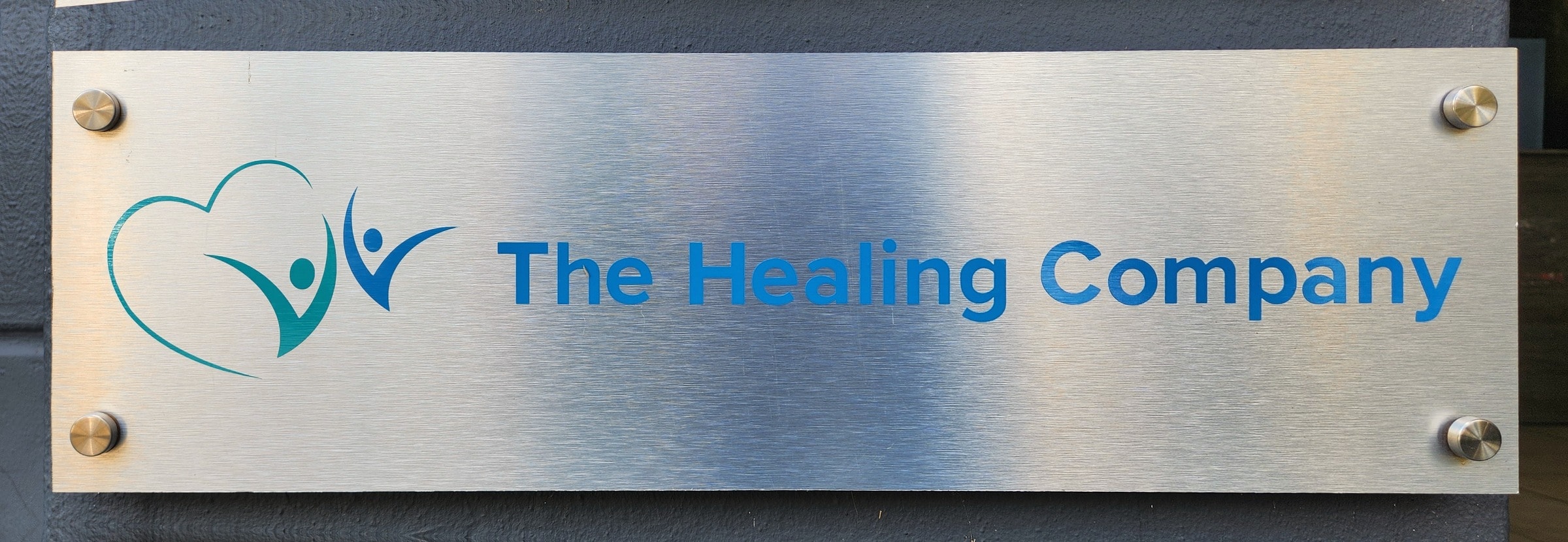 The Healing Company's brushed metal sign on the wall outside